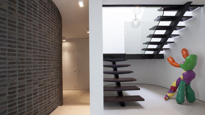 L’escalier sculptural dessine une colonne vertébrale. Sa rampe en verre transparent discrète met en valeur sa structure peinte en noir.