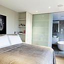 La chambre est séparée de la salle de bains par une porte coulissante en verre sablé qui cache, lorsqu’elle est ouverte, une bibliothèque. Au mur, une photo de Sébastien Patron.