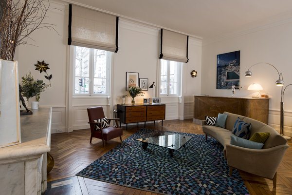 Dans le salon de l’appartement d’Anne-Charlotte Arminjon, canapé en arc de cercle et fauteuil en cuir vintage. Tapis, Golran. A droite, sur le comptoir bar des années 1930, lampe vintage Serpente créée en 1965 par Elio Martinelli (à vendre). Au dessus, photo originale de l’Hôtel du Cap-Eden-Roc au Cap d’Antibes réalisée par Slim Aarons en 1973. Entre les deux fenêtres décorées de stores en lin gansés de soie sauvage, partie d’un meuble en bois avec plateau et côtés repeints en noir.