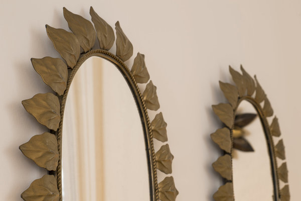 Gros plan sur un duo de miroirs ovales encadrés d’un décor de feuilles en métal doré vieilli et patiné.