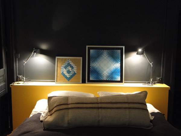Dans la même chambre, ambiance différente et plus graphique avec des œuvres encadrées de Vasarely et un gros coussin en lin brut animé d’une rayure tissée.