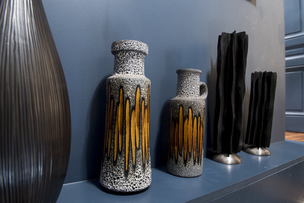 De part et d’autre de deux céramiques à la texture mouchetée, un vase et des photophores actuels en résine en contraste sur un mur bleu canard.