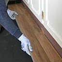 Etape 3 : pose de la première rangée de lames le long du mur dans un angle, avec des cales en morceaux de revêtement placées entre les lames et le mur pour obtenir un espace de dilatation. L’assemblage des lames se fait de la gauche vers la droite.