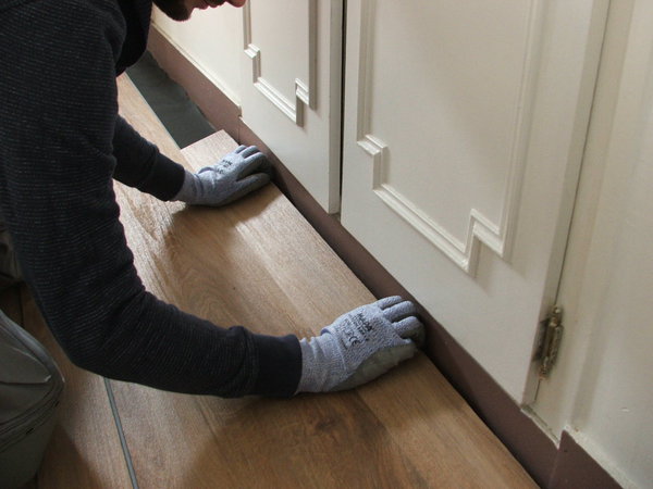 Etape 11 : découpe de la dernière rangée par report et assemblage pour terminer la pose. La dernière rangée assemblée, enlever les cales de revêtement de dilatation, couper l’excès de sous-couche le long des plinthes, et poser des plinthes coordonnées pour une finition parfaite.