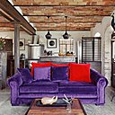 Le plafond avec voûtes recouvertes de terre cuite ancienne, la poutraison et le pilier en acier oxydé font référence à une architecture ancienne alors que la maison est neuve. Le canapé Chesterfield restauré est rehoussé avec un velours violet. Suspensions lumineuses, Tom Dixon.