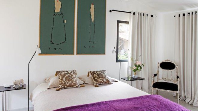 Chaise ancienne à la carcasse rehaussée à la feuille d’argent, assise et dossier recouverts de velours. Coussins en velours imprimés avec motifs retravaillés au pinceau. Luminaires et guéridons minimalistes. Au-dessus du lit, sérigraphies de Bernard Quesniaux.