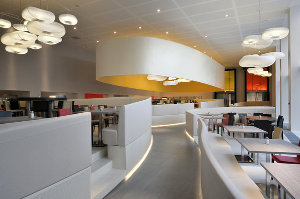 Le volume de la cafétéria est composé de trois espaces de forme organique délimités par des banquettes courbes, reprises au plafond par de grands abat-jour.