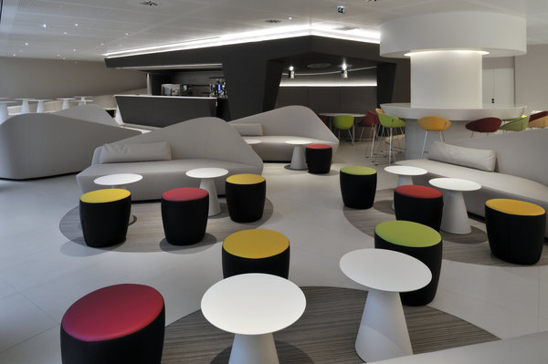 Le café contemporain offre de vastes espaces détente avec des banquettes aux formes sinueuses, des poufs colorés et des tables d’appoint basses comme dans un salon.