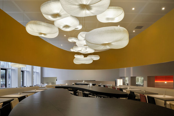 Des grandes tables d’hôtes de forme libre occupent la partie centrale de la cafétéria.