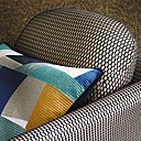 Coussin en satin de coton avec tissage d’inspiration géométrique déstructuré, coloris bleu 3919 04 19, existe en vert, mordoré et rouge. Fauteuil recouvert du tissu Reverso un voile graphique ajouré travaillé sur un métier à tricoter. Collection Molitor, collection automne-hiver 2017-18.