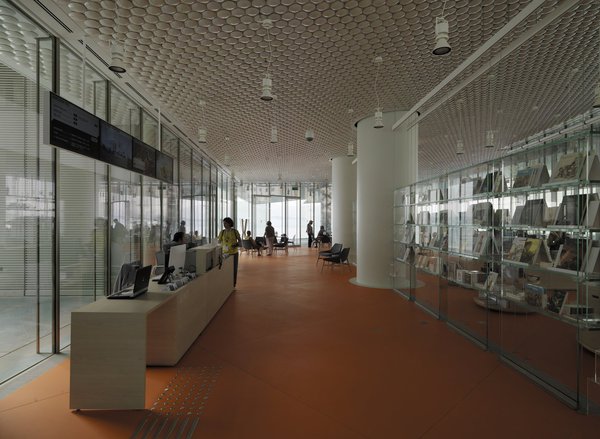 Au rez-de-chaussée, une façade entièrement transparente abrite un café, un restaurant, un magasin et un centre d'information. Ici, le plafond est recouvert de céramique, tandis que le sol est orange, se démarquant du pavé de béton bleu utilisé pour les espaces extérieurs.