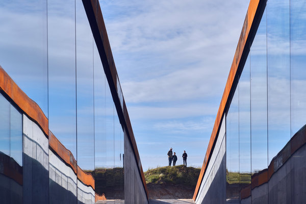 Les murs miroitants chapeautés d’acier patiné semblent sortir de la dune de terre et de sable.