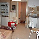 La cuisine avant : une pièce de vie maladroitement agencée avec un coin cuisine sans plan de travail implanté comme une verrue. Une décoration chargée, un espace encombré et trop meublé.