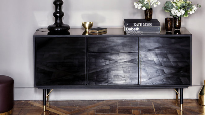 Cette enfilade fait office de buffet, meuble télé ou vaisselier pour y ranger les objets du quotidien. Sur toute la surface du dessus, une plaque de miroir teinté complète le caractère chic du meuble. Enfilade Miroir, chêne noir teinté mat qui laisse deviner les veinures du bois, pieds en laiton, 2290 €.