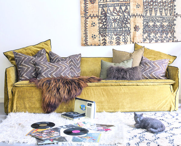 Maison de Vacances décline des créations textiles dans un esprit ethnique chic avec des motifs graphiques et de belles matières naturelles, peaux et fourrures. Sur le canapé, coussins imprimés wabi-sabi Zanzibar coloris havane (existe en coloris argile, grenat et indigo et forest.