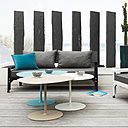 Tables basses Kona en aluminium caractérisées par une forme géométrique qui permet de les associer ensemble comme une mosaïque ou un puzzle (H 51 x 63 x 51,6 x 39,4 (pour le plateau). 20 couleurs disponibles. A droite, fauteuil Hegoa (H 64,5 x 97 x  hauteur totale 63 cm) avec montage et boulonnage apparent et assise extra basse en acier galvanisé. Garnissage avec coussins déhoussables en tissu spécial déperlant et résistant aux UV noir, blanc ou taupe et intérieur en mousse. Création Luc Jozancy.