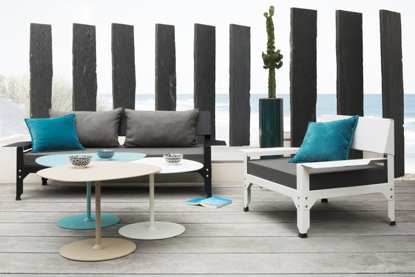 Tables basses Kona en aluminium caractérisées par une forme géométrique qui permet de les associer ensemble comme une mosaïque ou un puzzle (H 51 x 63 x 51,6 x 39,4 (pour le plateau). 20 couleurs disponibles. A droite, fauteuil Hegoa (H 64,5 x 97 x  hauteur totale 63 cm) avec montage et boulonnage apparent et assise extra basse en acier galvanisé. Garnissage avec coussins déhoussables en tissu spécial déperlant et résistant aux UV noir, blanc ou taupe et intérieur en mousse. Création Luc Jozancy.