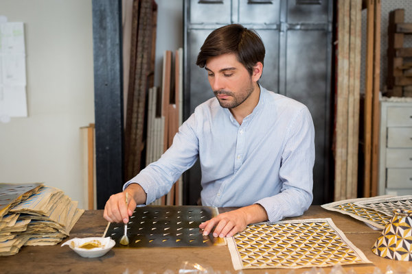 Après impression de la première couleur du motif, chaque feuille est colorée à la main à l’aide d’un pochoir. Ici, Vincent réalise la teinte jaune du décor n° 5.
