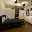 Une chambre en noir et blanc : lit Lipp Bed, création Piero Lissoni en 2015, éditée par Living Divani. Modèle avec tête de lit et repose-tête intégré en tissu ou cuir. Lampe de table Trépied, création Serge Mouille en 1954 rééditée par Editions Serge Mouille. Suspension à bras cassés Araignée, création Serge Mouille en 1954, rééditée par Editions Serge Mouilles. Lampadaire B211, création Michel Buffet en 1952 réédité par Lignes de Démarcation.