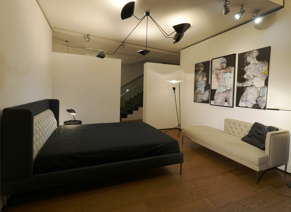 Une chambre en noir et blanc : lit Lipp Bed, création Piero Lissoni en 2015, éditée par Living Divani. Modèle avec tête de lit et repose-tête intégré en tissu ou cuir. Lampe de table Trépied, création Serge Mouille en 1954 rééditée par Editions Serge Mouille. Suspension à bras cassés Araignée, création Serge Mouille en 1954, rééditée par Editions Serge Mouilles. Lampadaire B211, création Michel Buffet en 1952 réédité par Lignes de Démarcation.