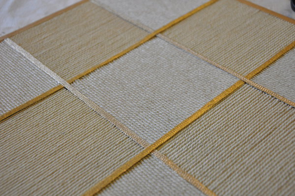 Gros plan sur un travail de damiers en cordes de lin bicolores rehaussés et sertis de galons, couleur ivoire et or. Collection Marqueté.
