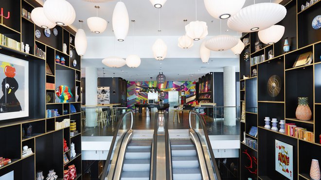 L’accès principal de l’hôtel citizenM la Défense se situe au rez-de-jardin et on accède à la réception informelle (on s’enregistre soi-même sur les comptoirs) par les escalators.