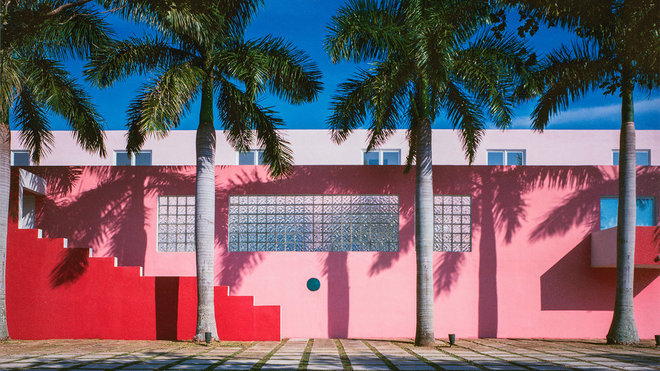 La piscine intérieure centrale de la Pink House, construite à Miami, se laisse deviner à travers le hublot unique de son mur d’entrée située sous la fenêtre horizontale en dalles de verre. Réalisation Arquitectonica.