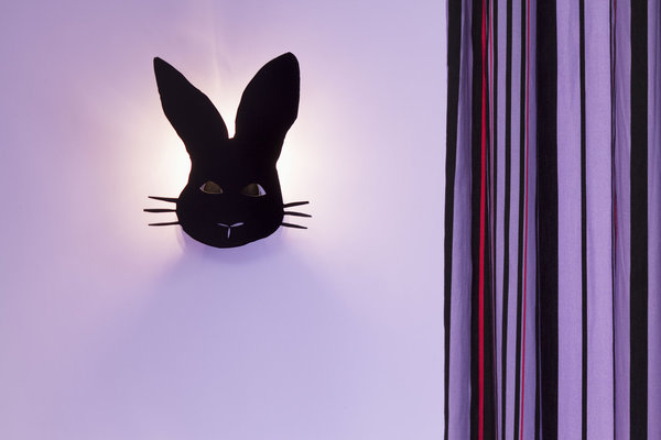 Détail d’une applique lumineuse, dessiné comme un masque de fête.