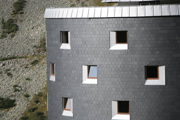 Façade en arrondi recouverte d’ardoises carrées qui jouent avec la lumière et dessinent une seconde peau.