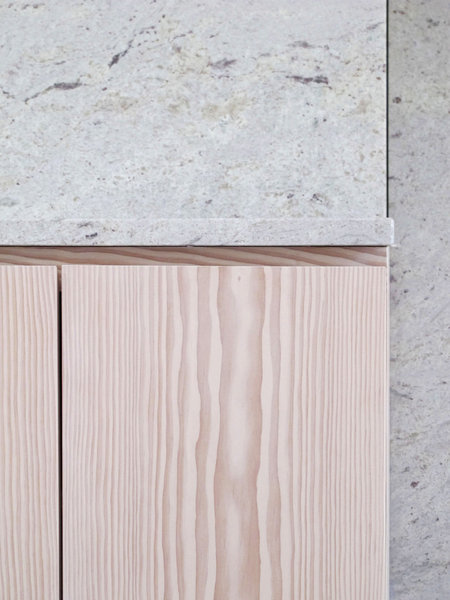 Détail du granit coloris cachemire blanc en association avec le douglas lasuré blanc. Les portes des rangements de la cuisine sont équipées de gorges et prises de main pour offrir des façades discrètes.