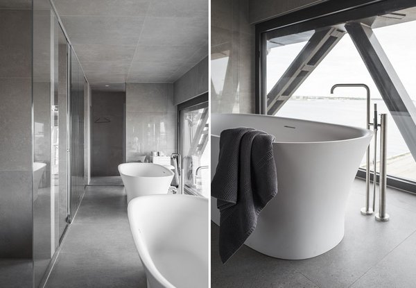 Nappée d’un dallage de pierre naturelle, la salle de bains est dotée d’une baignoire en îlot, se reflétant dans un miroir, Elle offre un mur entièrement vitré sur le port.