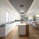 La cuisine offre un îlot avec une hotte intégrée dans le plafond qui fait office de séparation entre la zone de préparation des repas et la salle à manger. Le plan de travail en granit noir contraste avec les meubles sans poignée (un modèle personnalisé et adapté de la marque danoise Kvik).