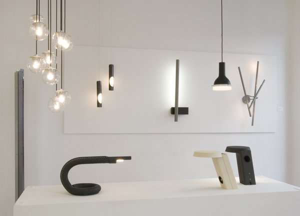 En bas, à droite, lampes de table noire et blanche, n° 607, en métal laqué, créées en 1971. A gauche, lampe à poser n° 536, en métal laqué, créée en 1966. En haut de gauche à droite, plafonnier n° 2095/9, en métal laqué, aluminium et verre, créé en 1958. Avec globes de 14 cm de diamètre. Deux suspensions tubulaires en métal laqué et verre créées en 1950. Au centre, applique minimaliste, en métal laqué, créée en 1954. A droite, applique n° 192, créée en 1950.