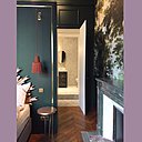 Derrière la cloison qui fait aussi office de tête de lit, une salle de bains déploie son espace dans le volume de suite parentale. La cheminée en marbre vert et mise en valeur par les tons du papier-peint et de la peinture couleur paon.