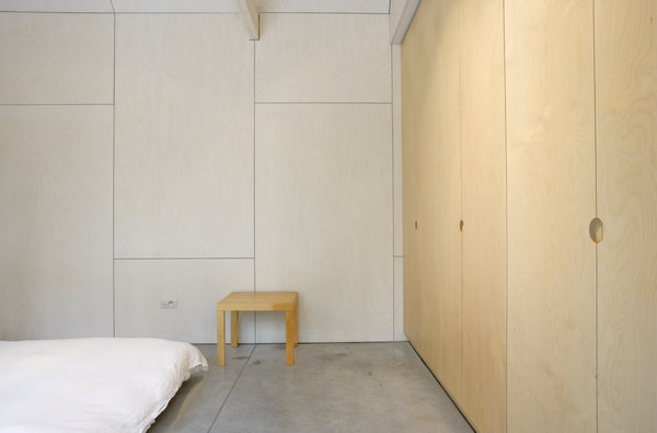 Les rangements intégrés en bois naturel tapissent les murs revêtus de panneaux de bois multiplex teintés blanc.