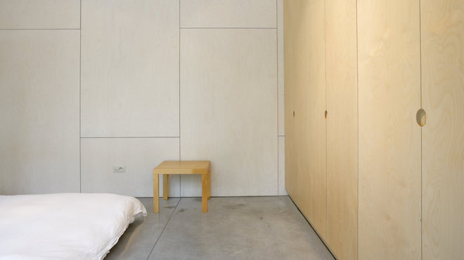 Les rangements intégrés en bois naturel tapissent les murs revêtus de panneaux de bois multiplex teintés blanc.