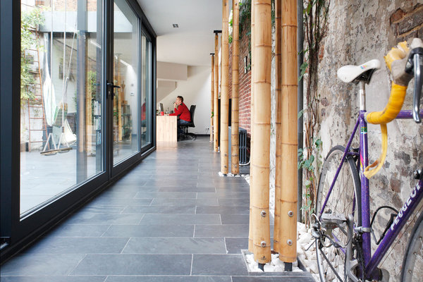 A l’intérieur, derrière la façade vitrée, les troncs des cannes de bambou, comme des arbres, s’associent à la végétation grimpante de l’ancien mur conservé.