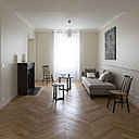 La seconde partie du salon profite d’une nouvelle cheminée ancienne en marbre rouge de style Louis XVI, chinée. Ses lignes sont plus droites que celles du modèle existant, une banale cheminée en marbre blanc jauni de style Louis XV. Devant, le tapis a été aussi refait pour s’harmoniser avec la nouvelle implantation. La décoration épurée met en valeur les traces du passé. Le raffinement des murs peints en crème et le plafond blanc immaculé créent un léger et subtil effet de contraste.