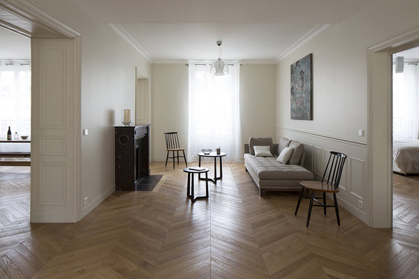 La seconde partie du salon profite d’une nouvelle cheminée ancienne en marbre rouge de style Louis XVI, chinée. Ses lignes sont plus droites que celles du modèle existant, une banale cheminée en marbre blanc jauni de style Louis XV. Devant, le tapis a été aussi refait pour s’harmoniser avec la nouvelle implantation. La décoration épurée met en valeur les traces du passé. Le raffinement des murs peints en crème et le plafond blanc immaculé créent un léger et subtil effet de contraste.