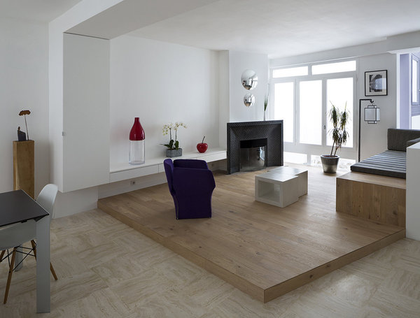 Le coin salon décloisonné est aménagé sur une estrade en bois qui permet de délimiter cet espace tout en profitant visuellement de tout le volume et d’ouvrir la perspective. Dans l’alignement de la poutre du plafond, on a aménagé un placard et, entre sa saillie et le conduit de cheminée, une console basse est suspendue. L’espace immaculé met en valeur la cheminée ancienne en fonte.