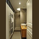 Aménagée derrière le mur de la cuisine, la salle de bains est très fonctionnelle, sans place perdue. Façon couloir avec dégagement, elle offre une grande douche avec un receveur rehaussé par une marche et une porte en verre pour éviter les éclaboussures.