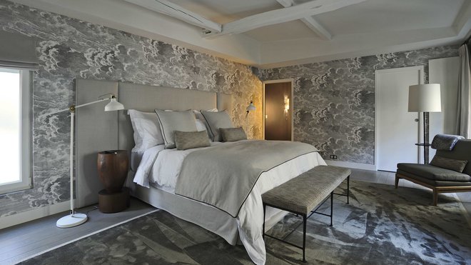 La chambre est tapissée avec le papier-peint onirique Nuvole, collection Fornasetti chez Cole and Son. Tapis en soie, Limited Edition. Table de nuit, Chris Lehrecke pour la Galerie Ralph Pucci International. Au pied du lit, banc à l’assise recouverte d’un tissu Hermès par Dedar et fauteuil, Christian Liaigre.