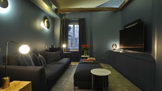 Le sol du salon TV feutré est recouvert d’une moquette vert olive qui s’assoie à des murs couleur bleu canard. Canapé, banquette et guéridons en marbre, B et B Italia. Coussins, Caravane et Hermès. Appliques murales lumineuses, Galerie Negropontes.