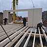Photo de chantier : mise en place du panneau de façade sur la structure bois. Elle est constituée de section de bois en sapin massif qui compose un plancher massif de gîtes et poutres.
