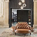 A droite, l’entrée cochère de l’ancien immeuble compose un hall monumental à partir duquel sont distribués les différents espaces. La banquette centrale structure l’espace comme un rond point. A gauche, tapis en patchwork et fauteuils en rotin pour le coin bibliothèque.