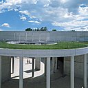 Pelouse flottante avec plateforme montée sur piliers et accès à la place centrale elliptique.