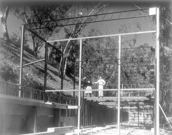 Un couple emblématique et une œuvre à 4 mains : Charles et Ray Eames qui ont révolutionné le design, posant sur la structure en acier de la Casa Study House n° 8, symbole de leur passion commune pour la modernité, qu’ils ont occupé à partir de 1949. Modern Print.