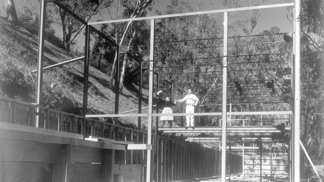 Un couple emblématique et une œuvre à 4 mains : Charles et Ray Eames qui ont révolutionné le design, posant sur la structure en acier de la Casa Study House n° 8, symbole de leur passion commune pour la modernité, qu’ils ont occupé à partir de 1949. Modern Print.