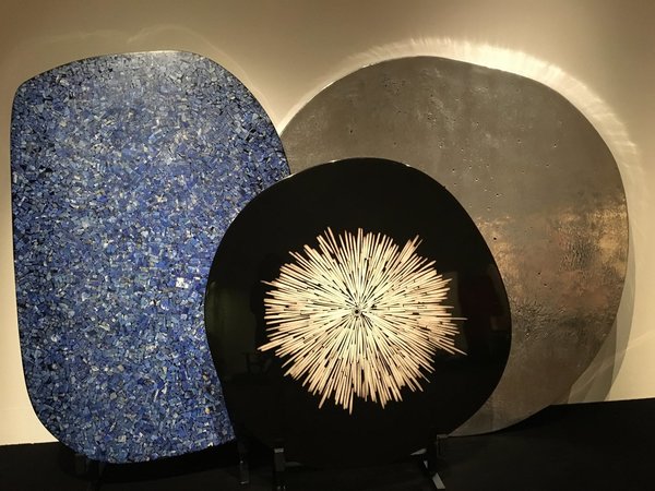 Lors de l’exposition bruxelloise à Bozar, organisée du 18 août au 24 septembre 2017, trois plateaux de table : devant, table « Cible » avec décor central en os créée, en 2011, à gauche, table « Mosaïque » en lapis lazuli, créée en 2008, et à droite, table « Lunaire » en aluminium moulé, création Chale Collection en 2008.