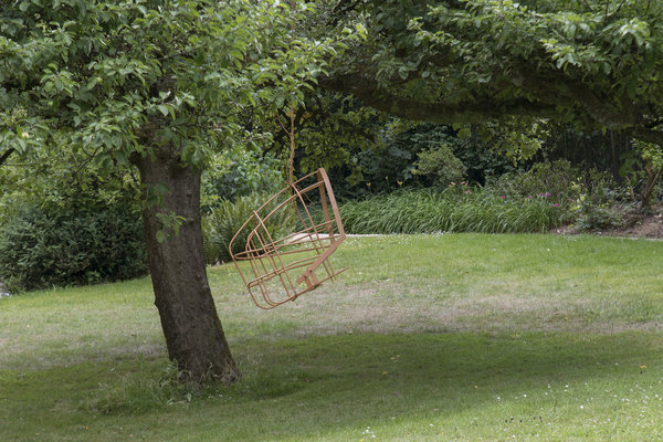 Accrochée dans le verger, nacelle balançoire en métal de récupération évoquant une muselière suspendue dans les airs. Œuvre « Servir l’homme ou comment servir l’homme » de Tanguy Poujol.